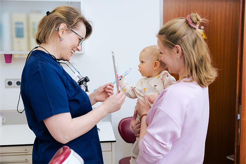 Eine junge Frau hält ihr Baby auf dem Arm und unterhält sich mit Dr. Weilandt.