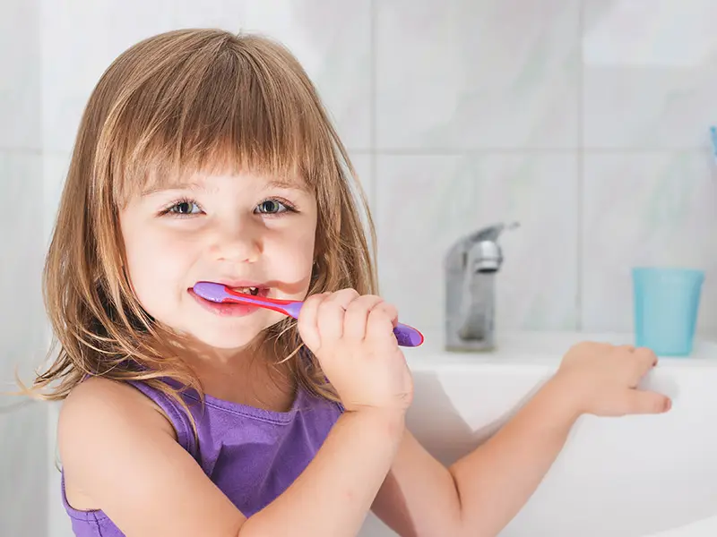 Ein kleines Mädchen übt das Zähneputzen. Denn die Pflege der KInderzähne ist wichtig für die Gesundheit.