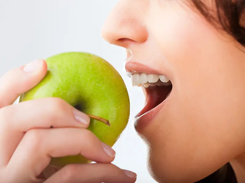 Eine Frau beißt in einen grünen reifen Apfel.