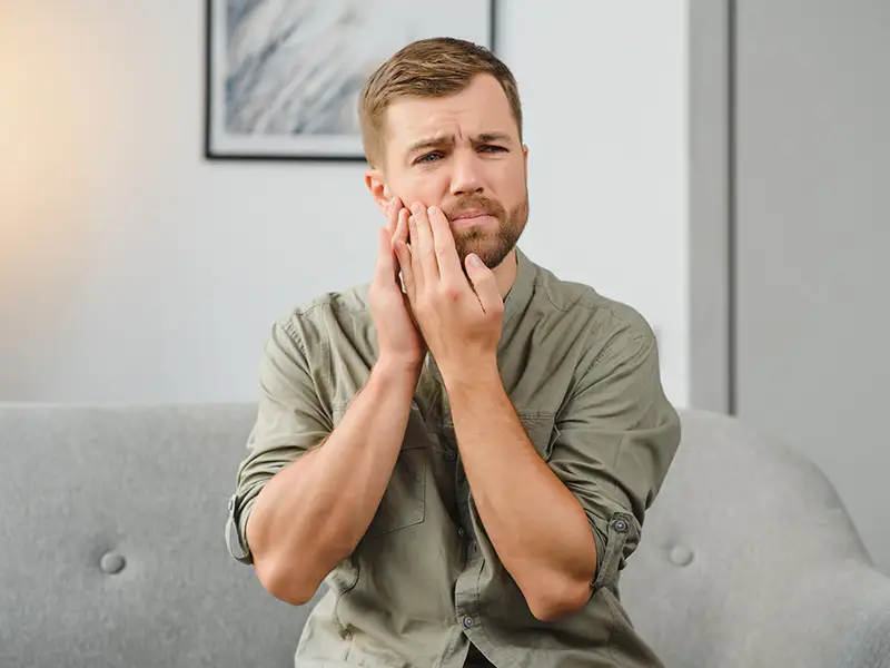 Ein junger Mann hält sich die Wange und hat Schmerzen.